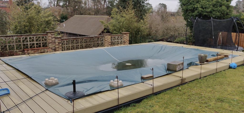Oval pool with decking and rectangular tarpaulin being used as winter cover